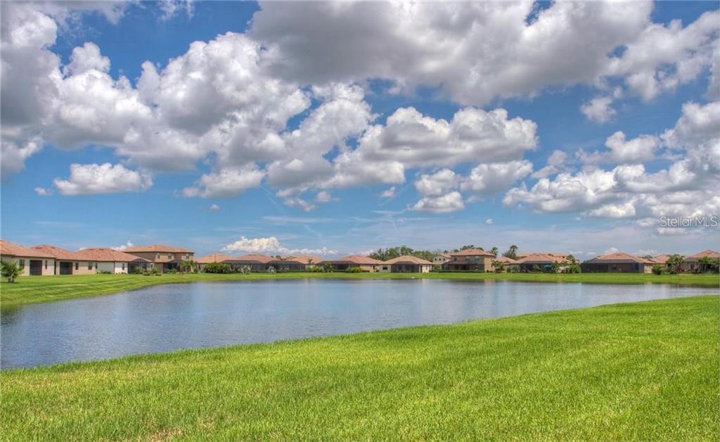 A grassy lawn overlooks a pond with a row of suburban houses in the background — 218 WHISPERING PALMS LANE, BRADENTON, FL