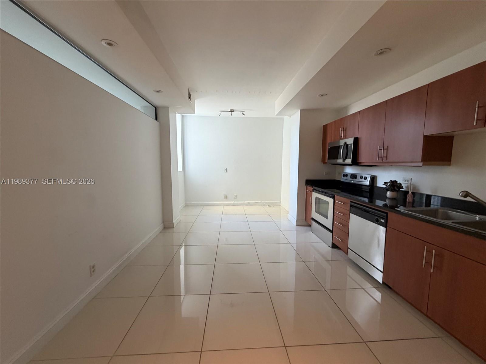 A kitchen with wood cabinets, stainless steel appliances, and white tile flooring — 111 E Flagler St # 606, Miami FL 33131, MIAMI, FL