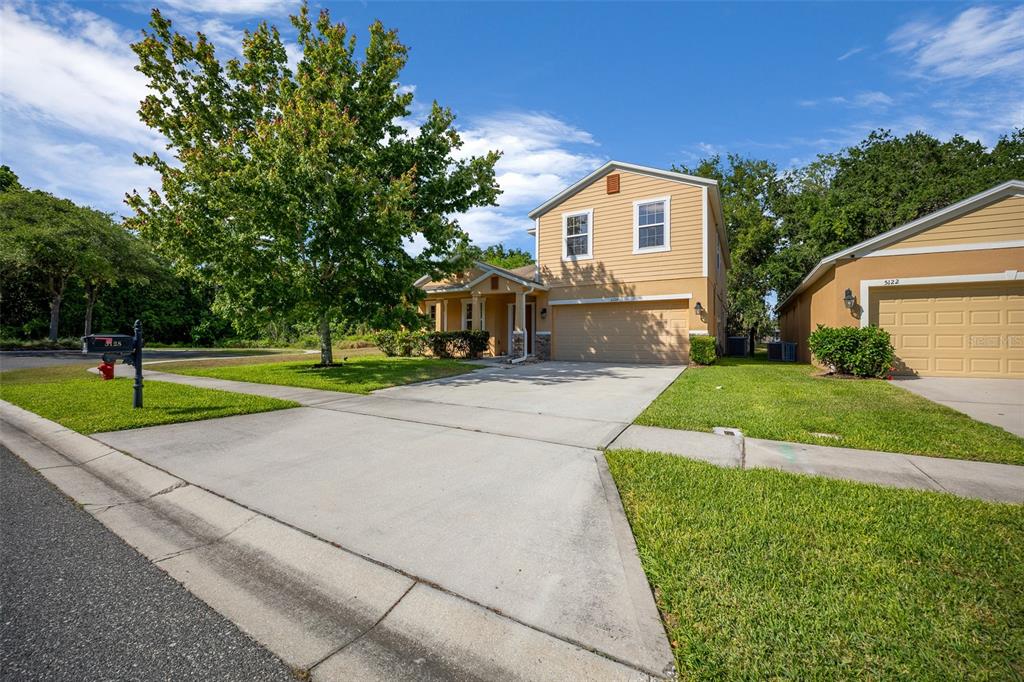 A two-story tan house with a concrete driveway and a large tree in the yard — 5128 GRASSY KNOLL DRIVE, TAVARES, FL