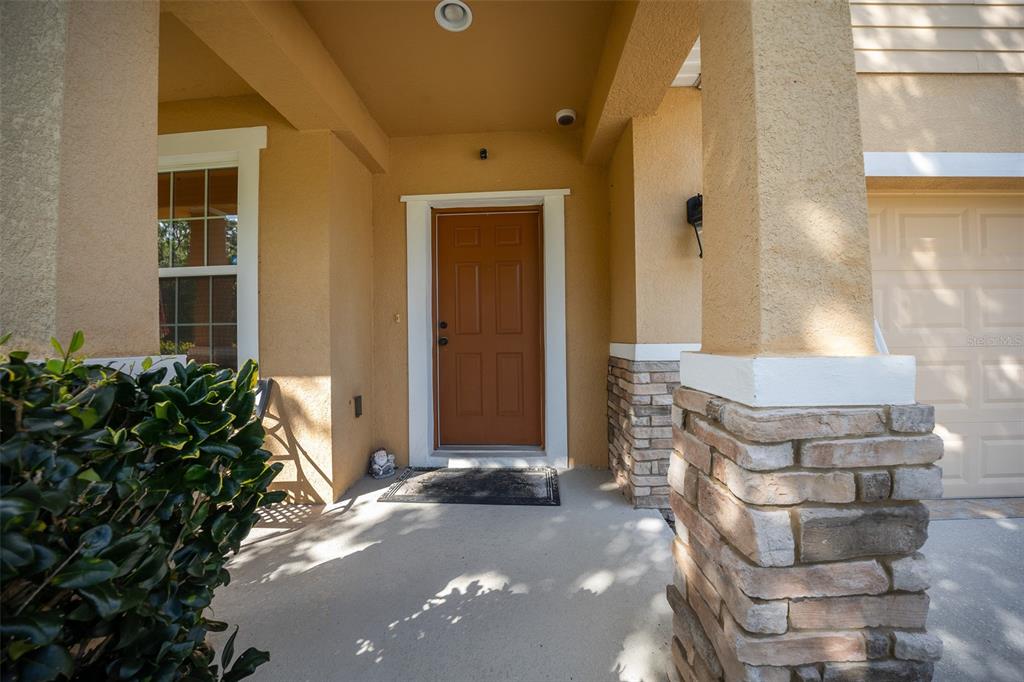 A covered front porch features a brown door, stone accents, and a beige stucco exterior — 5128 GRASSY KNOLL DRIVE, TAVARES, FL