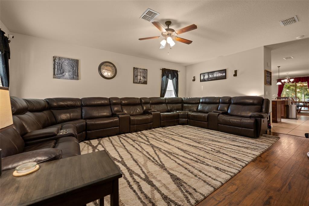 A large living room features a dark leather sectional sofa on a patterned area rug — 5128 GRASSY KNOLL DRIVE, TAVARES, FL