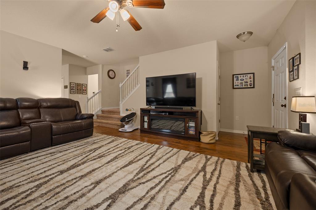 A living room features a large brown leather sofa, a patterned rug, and a television console — 5128 GRASSY KNOLL DRIVE, TAVARES, FL