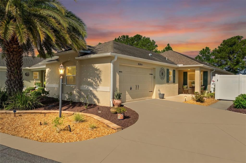 A single-story house with a beige stucco exterior, a two-car garage, and a palm tree — 16844 SE 91ST PHILLIPS COURT, THE VILLAGES, FL