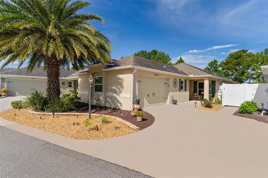 A tan single-story house with a palm tree, a two-car garage, and a paved driveway — 16844 SE 91ST PHILLIPS COURT, THE VILLAGES, FL