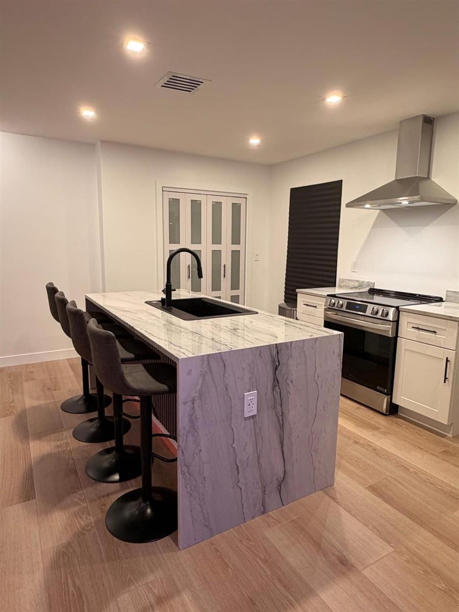 A modern kitchen features a marble-topped island with bar stools and stainless steel appliances — 1025 NW 148th Street, Miami FL 33168, MIAMI, FL