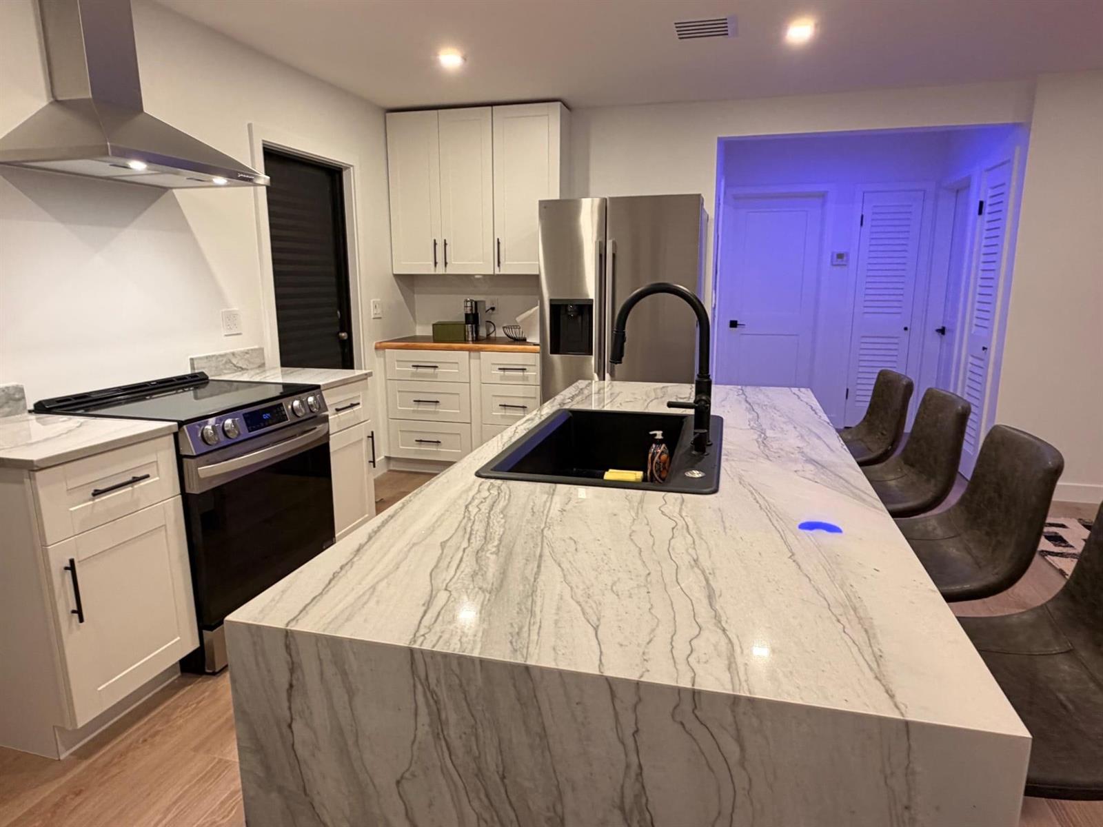 A modern kitchen features a large waterfall island with a black sink and white countertops — 1025 NW 148th Street, Miami FL 33168, MIAMI, FL
