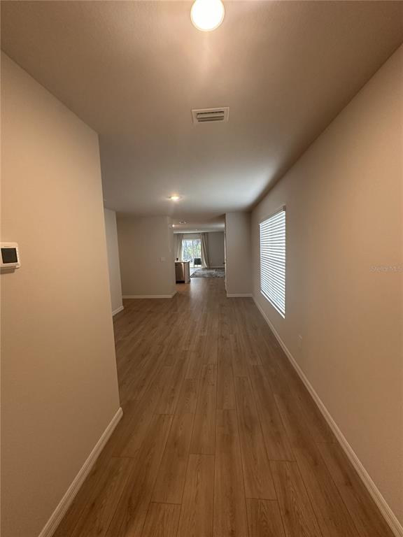 A hallway with light wood-look flooring leads toward an open-concept kitchen and living area — 10650 HIDDEN BANKS GLEN, PARRISH, FL