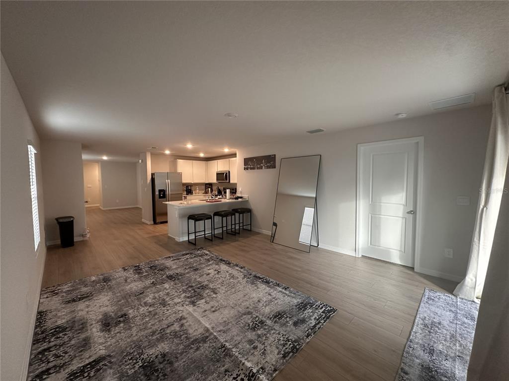 An open-concept living area features light wood flooring, a kitchen with bar seating, and rugs — 10650 HIDDEN BANKS GLEN, PARRISH, FL