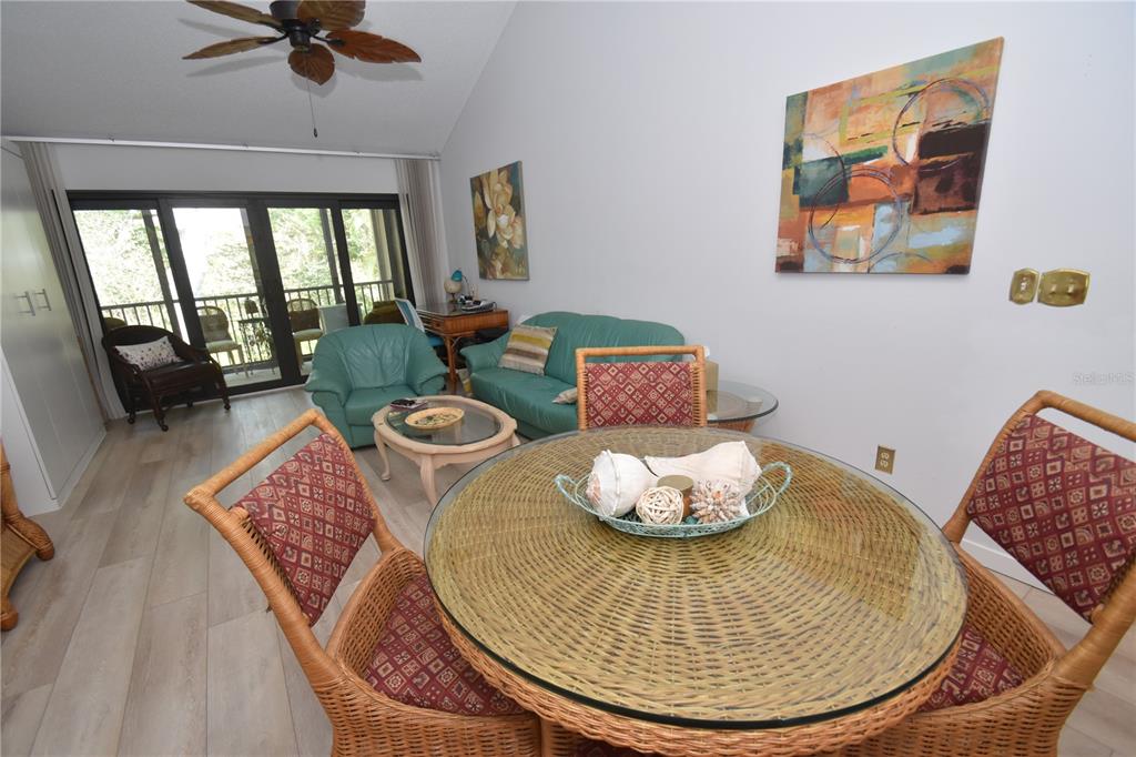 A living and dining area features a glass-topped wicker table, teal sofa, and vaulted ceiling — 1720 GLENHOUSE DRIVE UNIT GL429, SARASOTA, FL