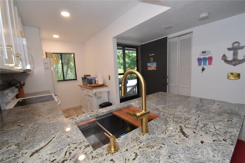 A kitchen features granite countertops, a gold faucet, a stainless steel sink, and white cabinets — 1720 GLENHOUSE DRIVE UNIT GL429, SARASOTA, FL