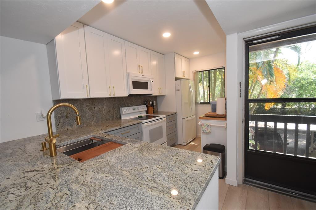 A kitchen features granite countertops, white upper cabinets, gray lower cabinets, and a sliding glass door — 1720 GLENHOUSE DRIVE UNIT GL429, SARASOTA, FL