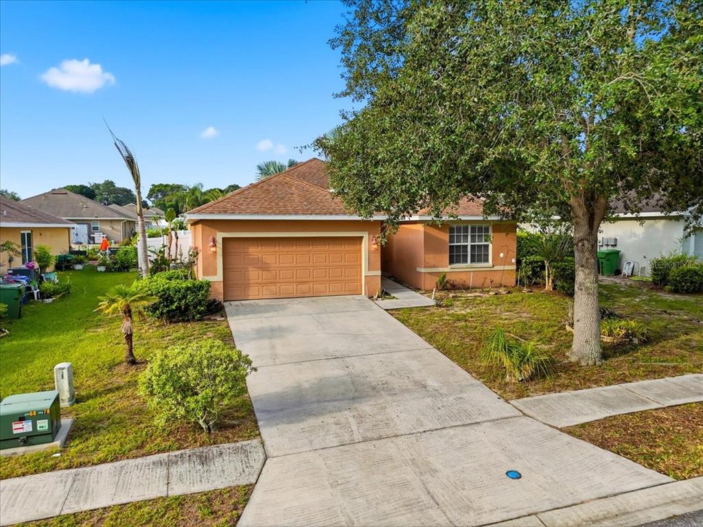 A single-story house with a tan stucco exterior, a two-car garage, and a large tree — 1966 WHITE HAWK WAY, WINTER HAVEN, FL