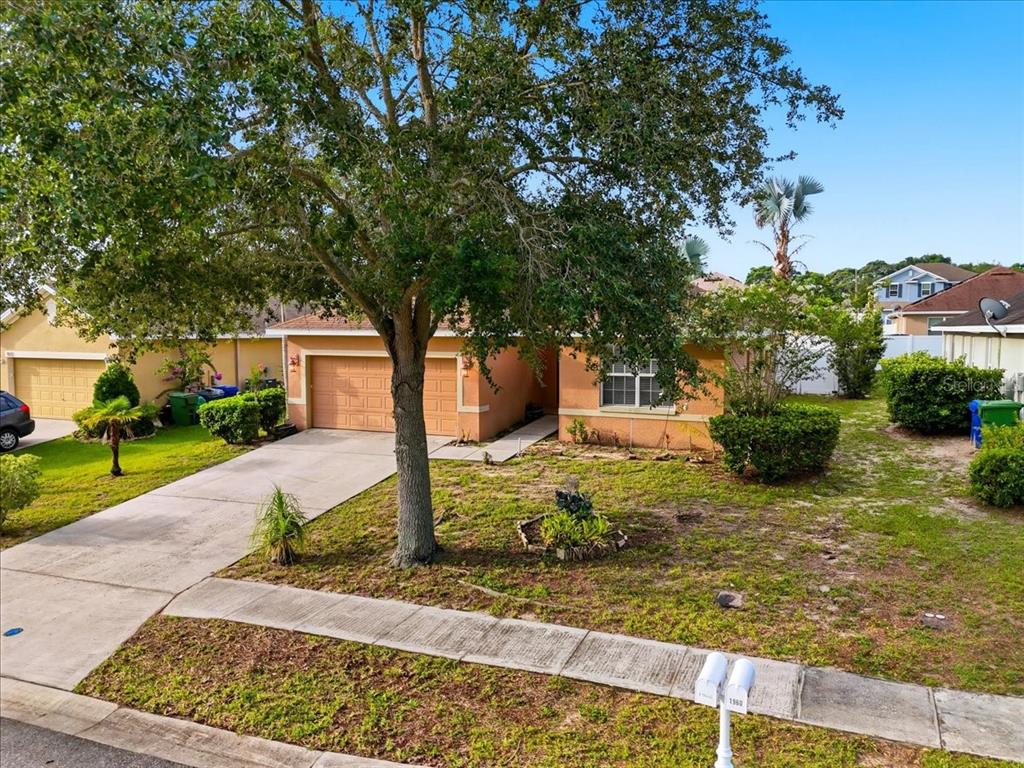 A single-story house with a tan exterior, a two-car garage, and a large front tree — 1966 WHITE HAWK WAY, WINTER HAVEN, FL