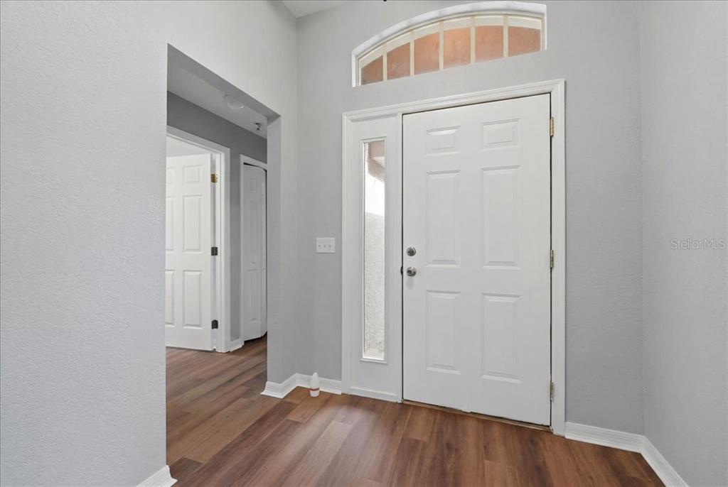 An entryway features a white front door with a sidelight, transom window, and wood flooring — 1966 WHITE HAWK WAY, WINTER HAVEN, FL