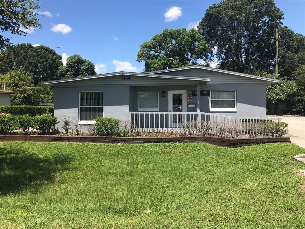 A single-story gray house features a front porch with a white railing and landscaping — 1334 S SEMORAN BOULEVARD, ORLANDO, FL