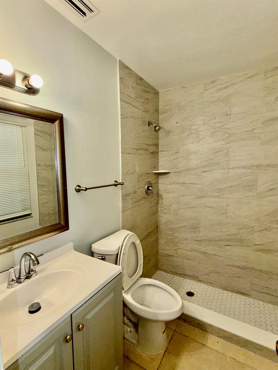 A bathroom features a vanity, a toilet, and a walk-in shower with tiled walls — 9392 Affirmed Lane, Boca Raton FL 33496, BOCA RATON, FL