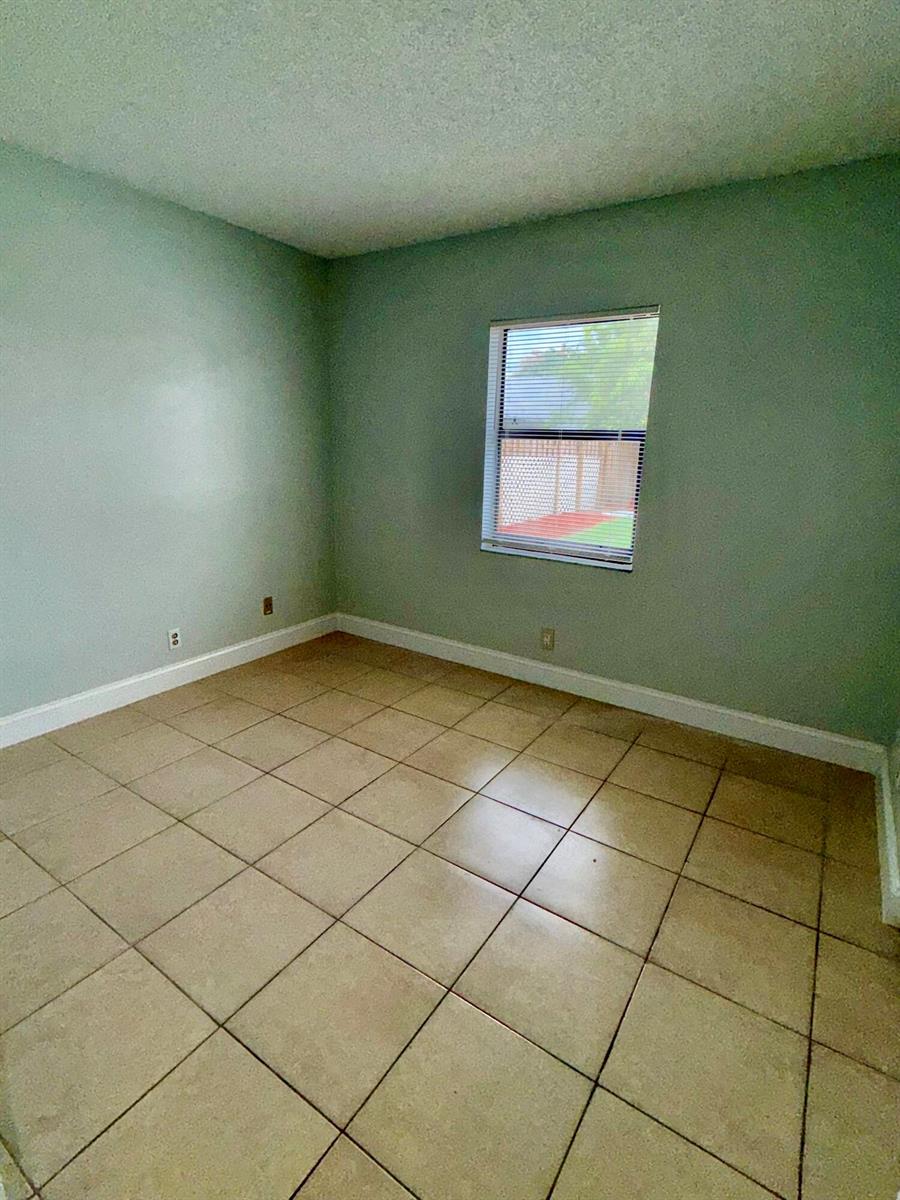 An empty room with light green walls, beige tile flooring, and a single window — 9392 Affirmed Lane, Boca Raton FL 33496, BOCA RATON, FL