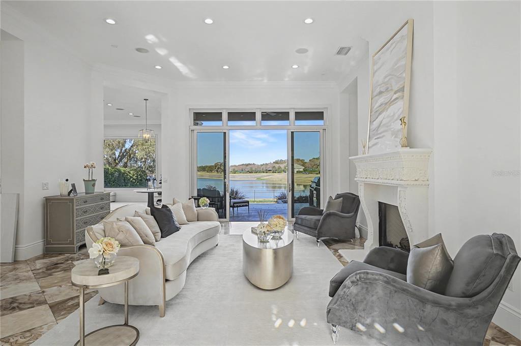 A bright living room features a curved sofa, fireplace, and sliding glass doors overlooking water — 2730 NW 80TH AVENUE, OCALA, FL