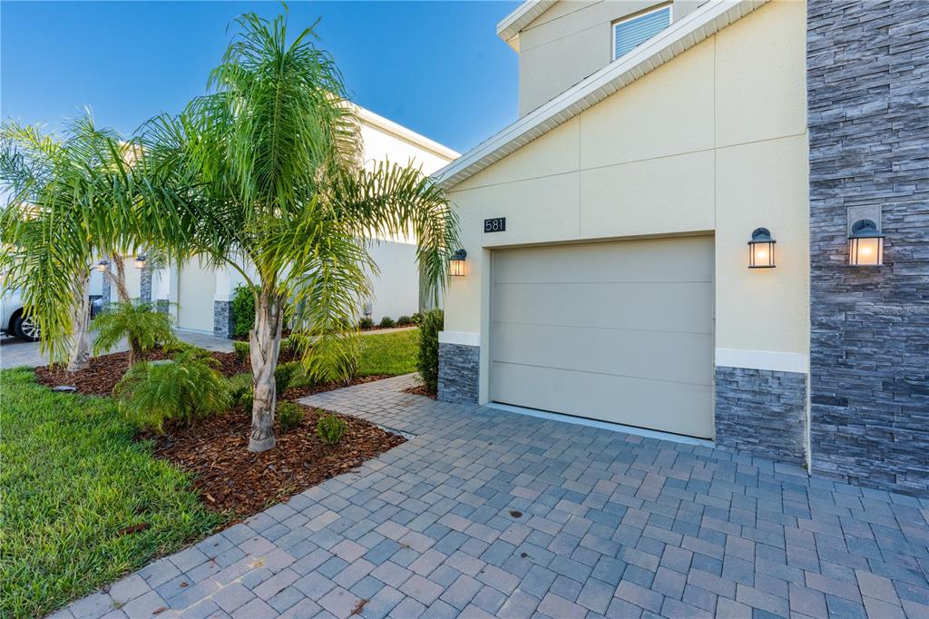 A paved driveway leads to a single-car garage with stone accents and a palm tree — 581 OCEAN COURSE AVENUE UNIT 581, DAVENPORT, FL