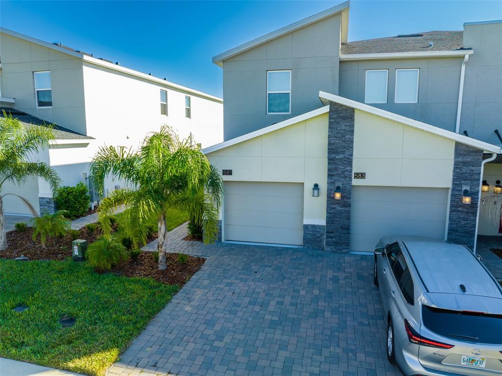 A view of two attached townhome garages with stone accents and a paved driveway — 581 OCEAN COURSE AVENUE UNIT 581, DAVENPORT, FL