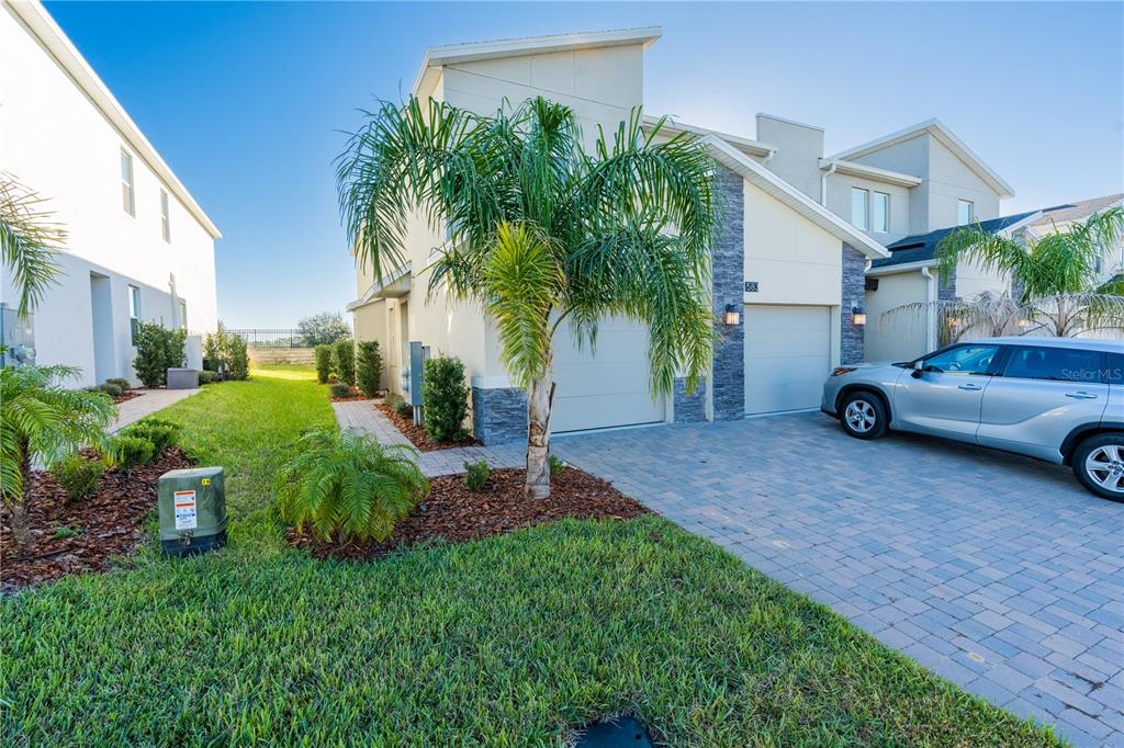 A two-story stucco townhouse with a stone facade, a paved driveway, and a palm tree — 581 OCEAN COURSE AVENUE UNIT 581, DAVENPORT, FL