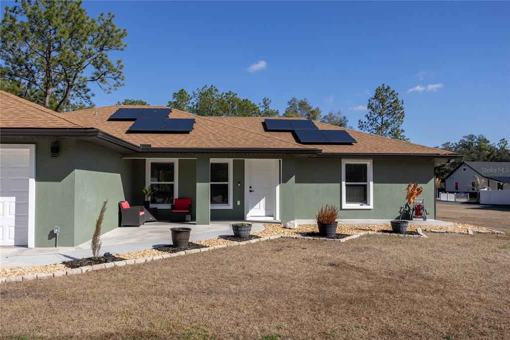 A single-story house with green stucco walls, a shingled roof with solar panels, and landscaping — 5793 SW 121ST TERRACE, OCALA, FL