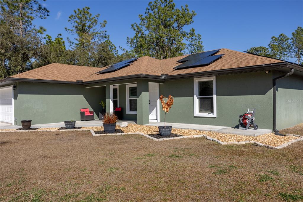 A single-story house with green stucco walls, a brown shingled roof, and solar panels — 5793 SW 121ST TERRACE, OCALA, FL