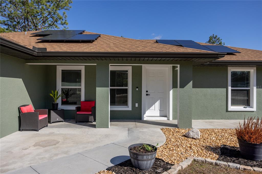 The exterior of a green house features a covered porch, white door, and solar panels — 5793 SW 121ST TERRACE, OCALA, FL