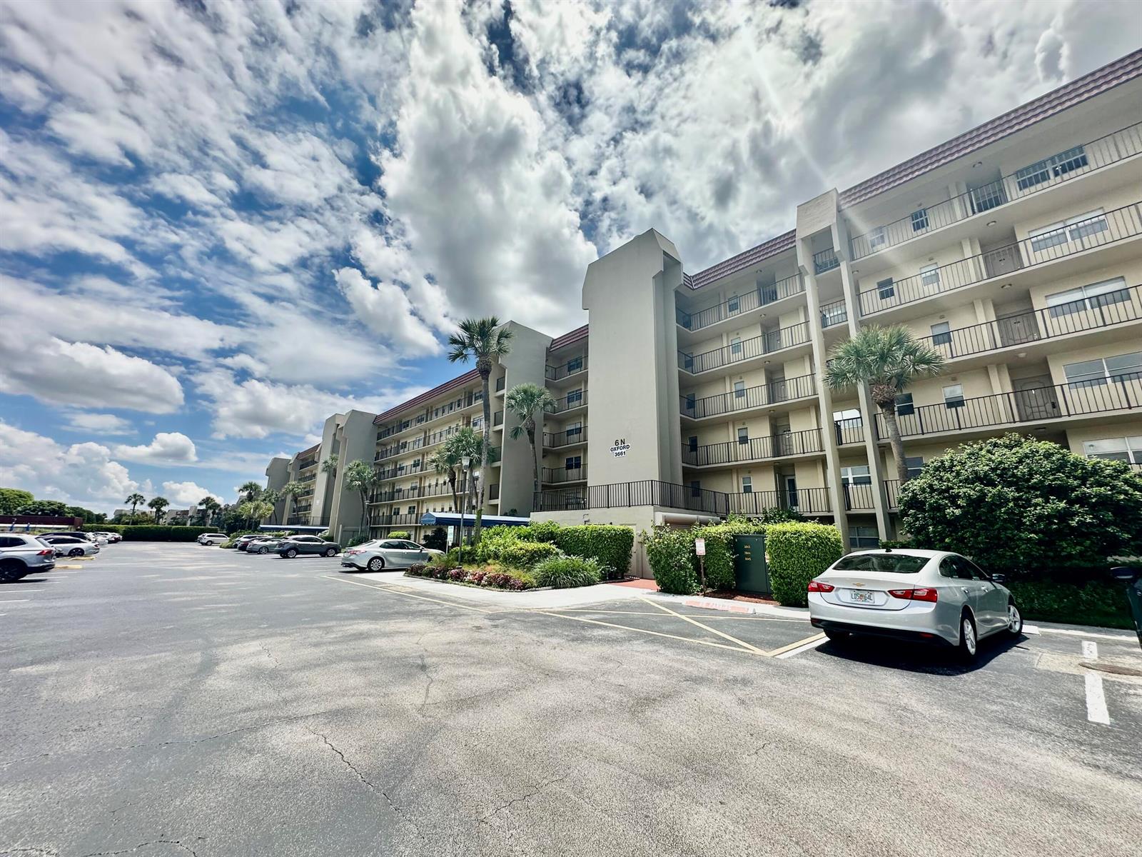 A multi-story apartment building features balconies and a large parking lot in front — 3661 Via Poinciana # 615, FL 33467, FL