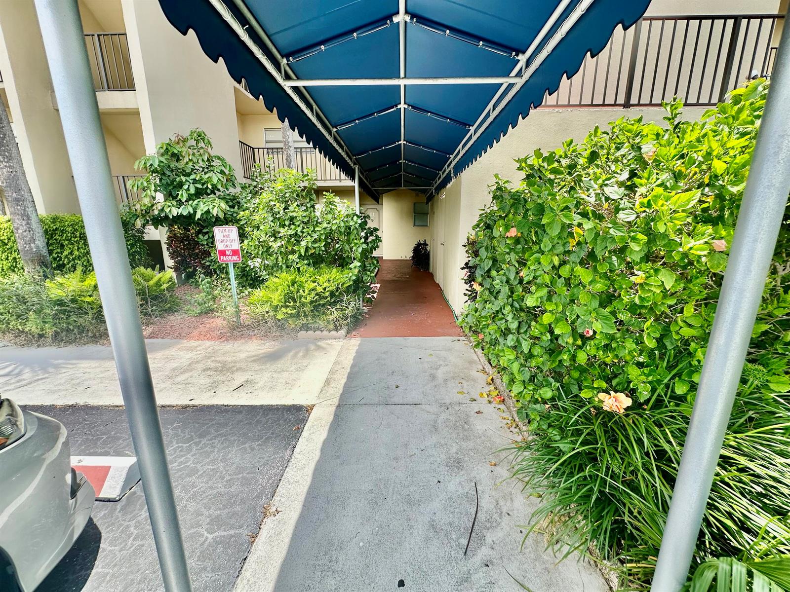 A covered walkway leads to an entrance between two large green bushes — 3661 Via Poinciana # 615, FL 33467, FL