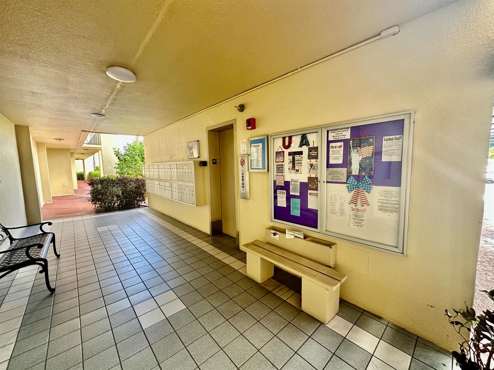 An outdoor apartment building hallway features a tiled floor, mailboxes, an elevator, and a bulletin board — 3661 Via Poinciana # 615, FL 33467, FL