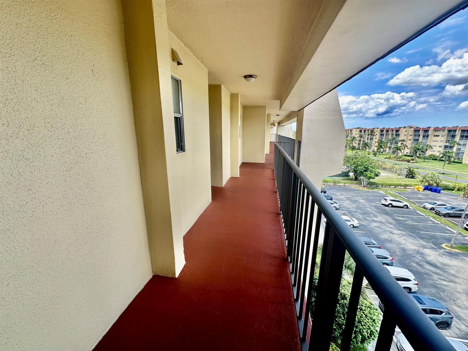 An outdoor balcony with a red floor and black metal railing overlooks a parking lot — 3661 Via Poinciana # 615, FL 33467, FL