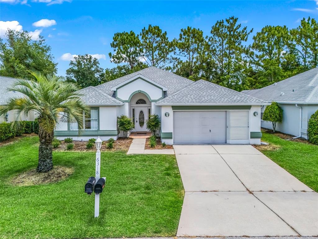 A single-story house with a white stucco exterior, green trim, and a concrete driveway — 6318 SW 117TH LOOP, OCALA, FL