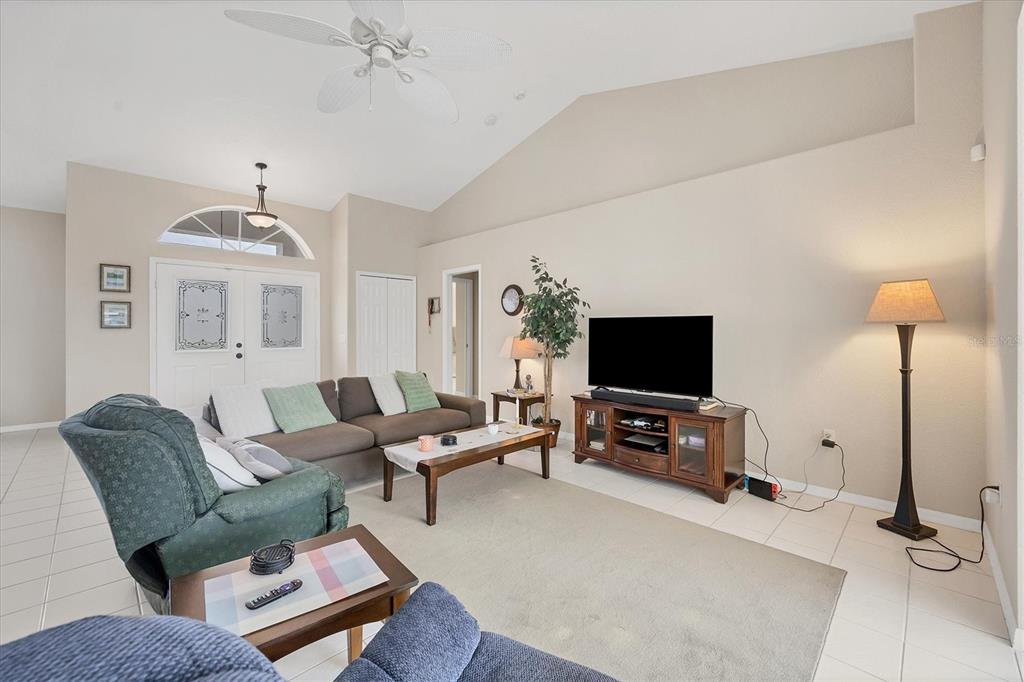 A living room features a vaulted ceiling, tile flooring, a sofa, and a television console — 102 MARKER ROAD, ROTONDA WEST, FL