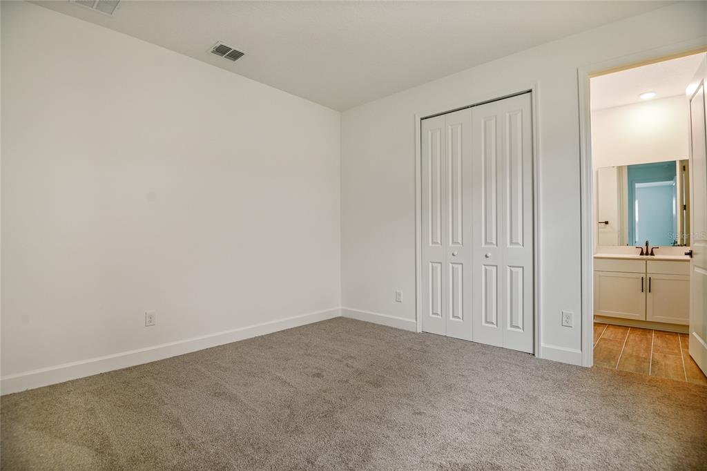 A bedroom with gray carpeting, white walls, a bi-fold closet, and an attached bathroom — 176 BLUE STAR COURT, TAVARES, FL
