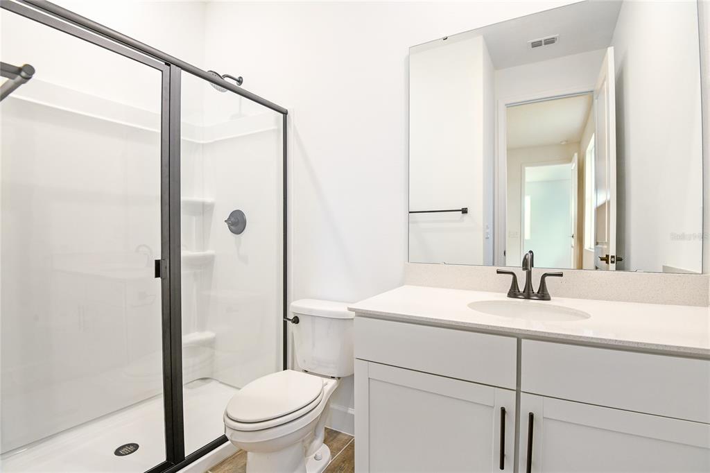 A bathroom features a white vanity, a toilet, and a glass-enclosed shower with black frames — 176 BLUE STAR COURT, TAVARES, FL