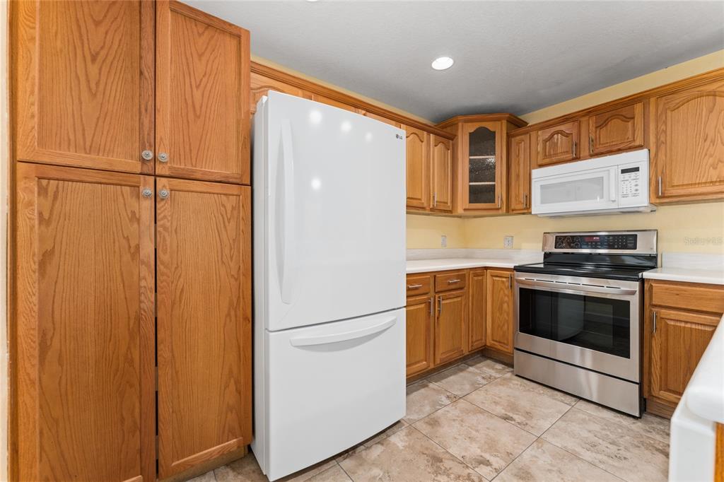 A kitchen with oak cabinets, a white refrigerator, stainless steel stove, and tiled flooring — 2613 S PARK AVENUE, TITUSVILLE, FL