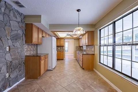 A kitchen with wood cabinets, tile floors, a stone wall, and a large window — 7528 RIVER COUNTRY DRIVE, WEEKI WACHEE, FL