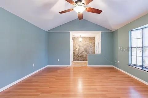 An empty room with light blue walls, wood flooring, a ceiling fan, and a stone accent wall — 7528 RIVER COUNTRY DRIVE, WEEKI WACHEE, FL