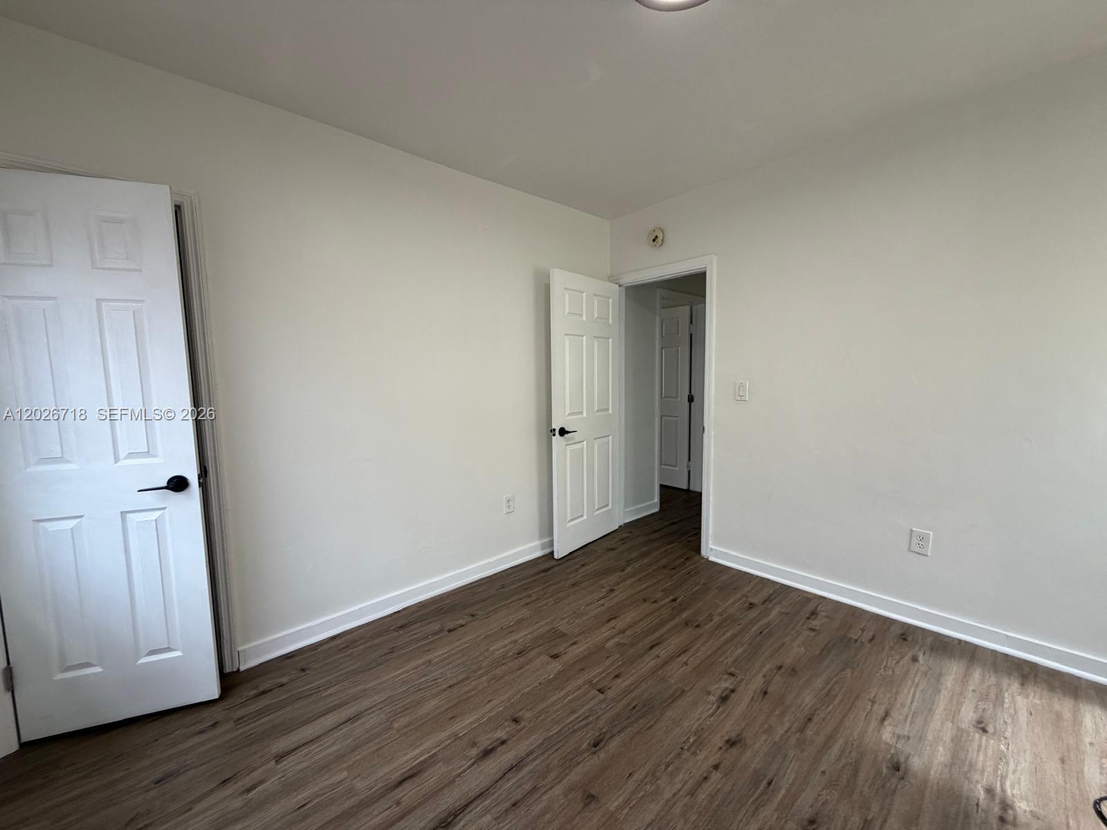 An empty room features white walls, wood-look flooring, and two open white interior doors — MIAMI, FL