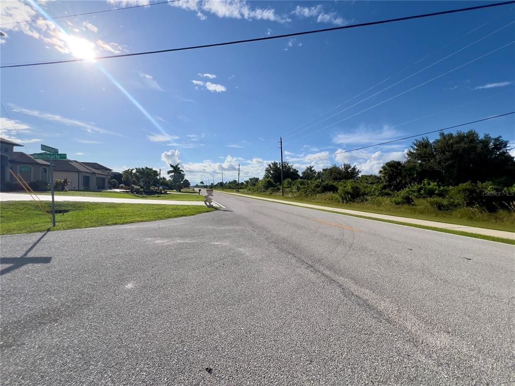 An asphalt road stretches into the distance past a street sign and residential landscaping — 14242 MONTMARTE AVENUE, PORT CHARLOTTE, FL