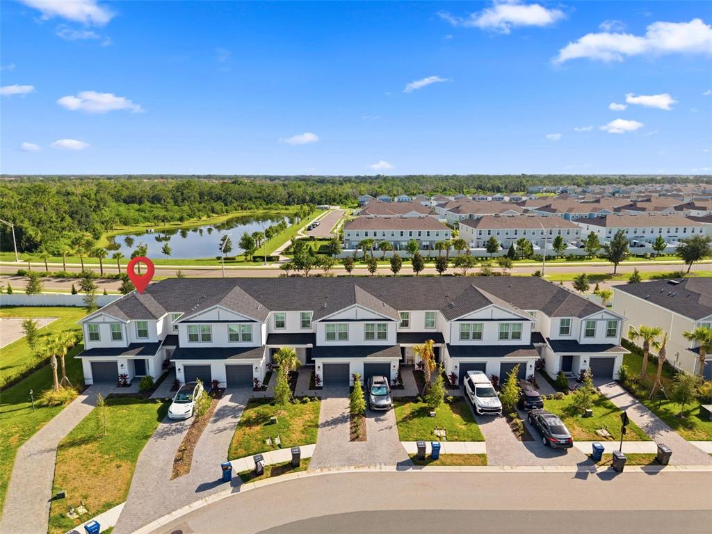 An aerial view shows a row of modern townhouses with driveways and a nearby pond — 14035 LILAC SKY TERRACE, BRADENTON, FL