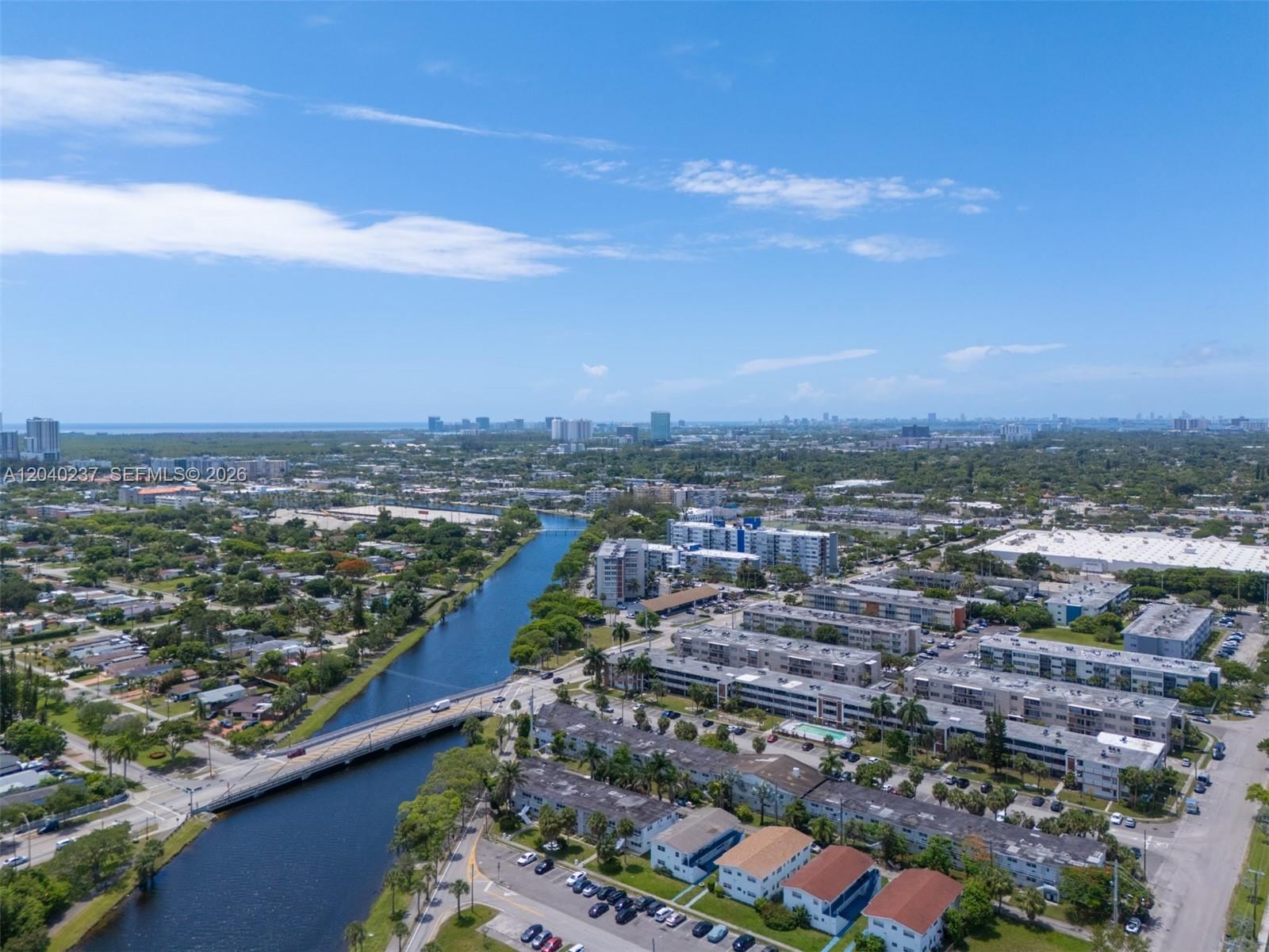An aerial view shows a canal flowing through a suburban area with apartment buildings — 1450 NE 170th St # 115, North Miami Beach FL 33162, NORTH MIAMI BEACH, FL