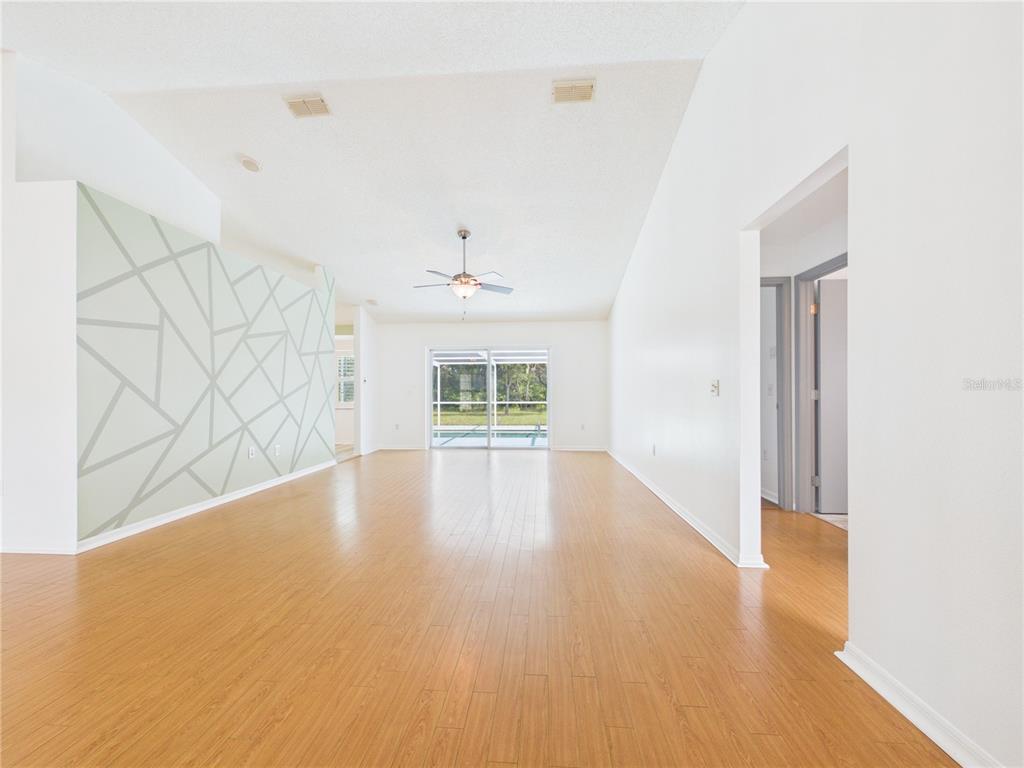 A spacious living room features light wood flooring, a geometric accent wall, and sliding glass doors — 9434 HOLNWON COURT, HUDSON, FL
