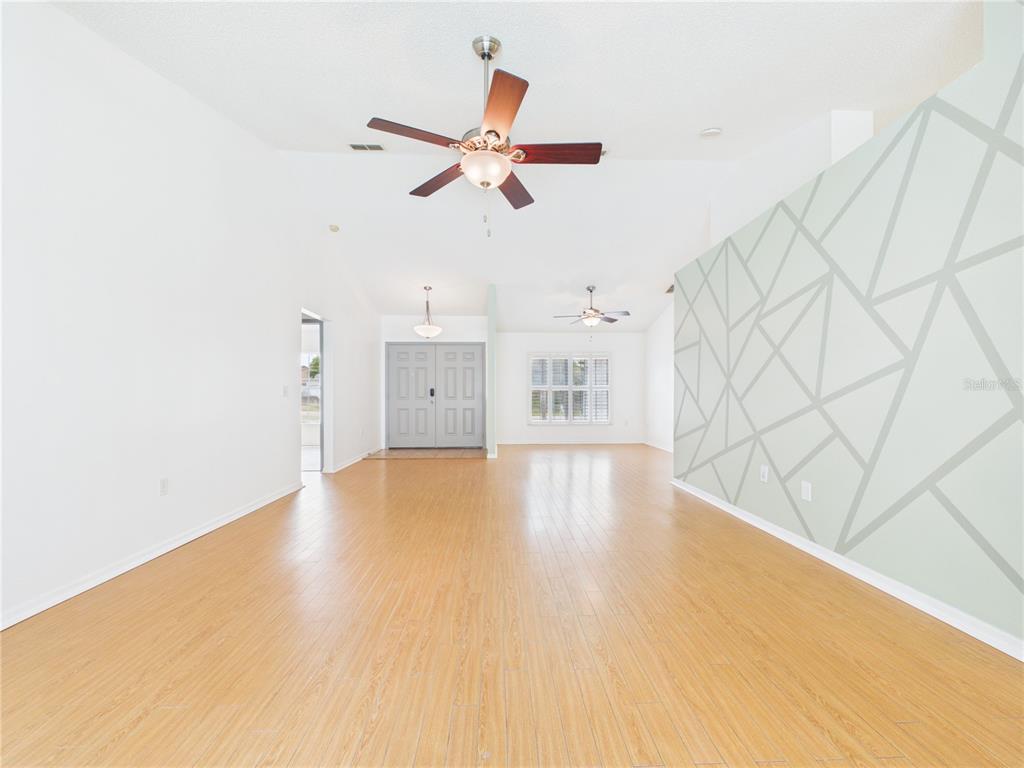 A spacious living area features light wood flooring, a geometric accent wall, and ceiling fans — 9434 HOLNWON COURT, HUDSON, FL