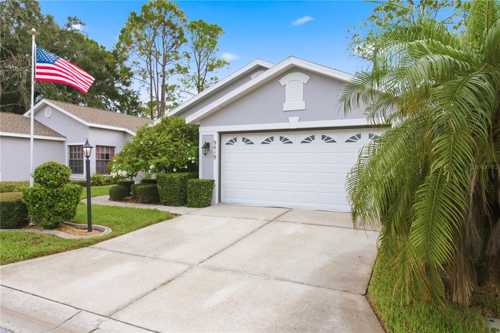 A single-story house with a white garage door, gray siding, and an American flag outside — 9419 GREEN NEEDLE DRIVE, NEW PORT RICHEY, FL