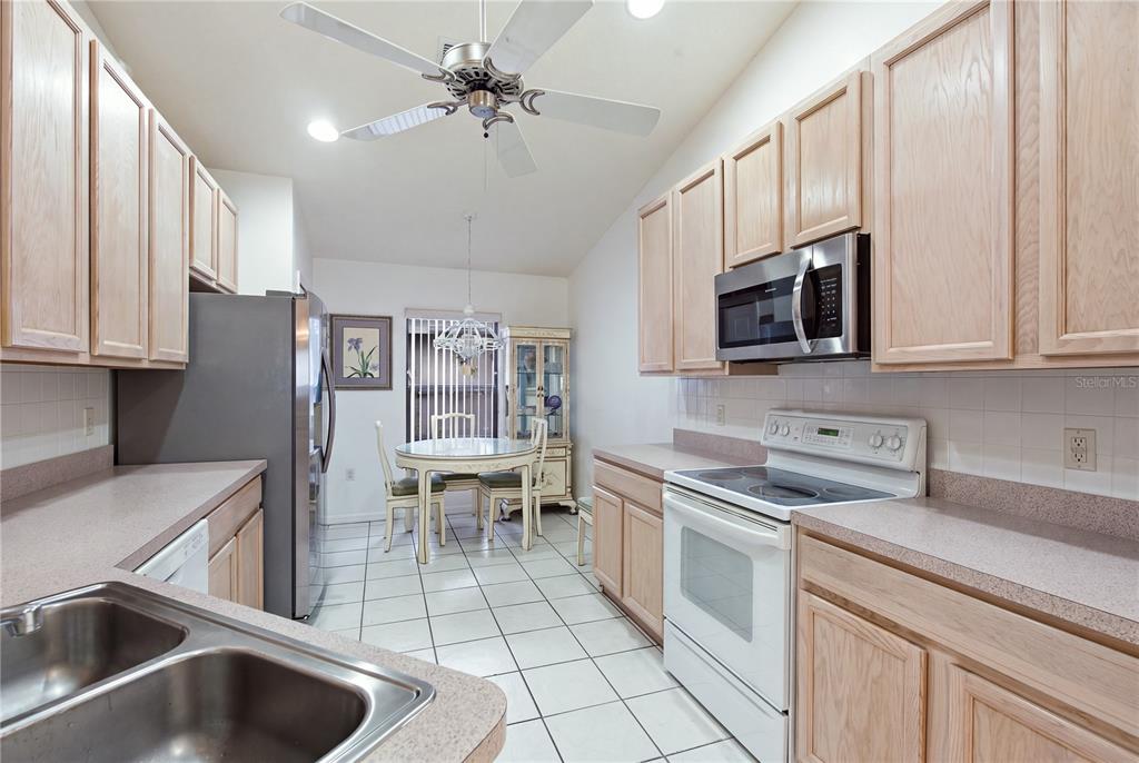 A kitchen with light wood cabinets, white appliances, tile flooring, and an adjacent dining area — 9419 GREEN NEEDLE DRIVE, NEW PORT RICHEY, FL