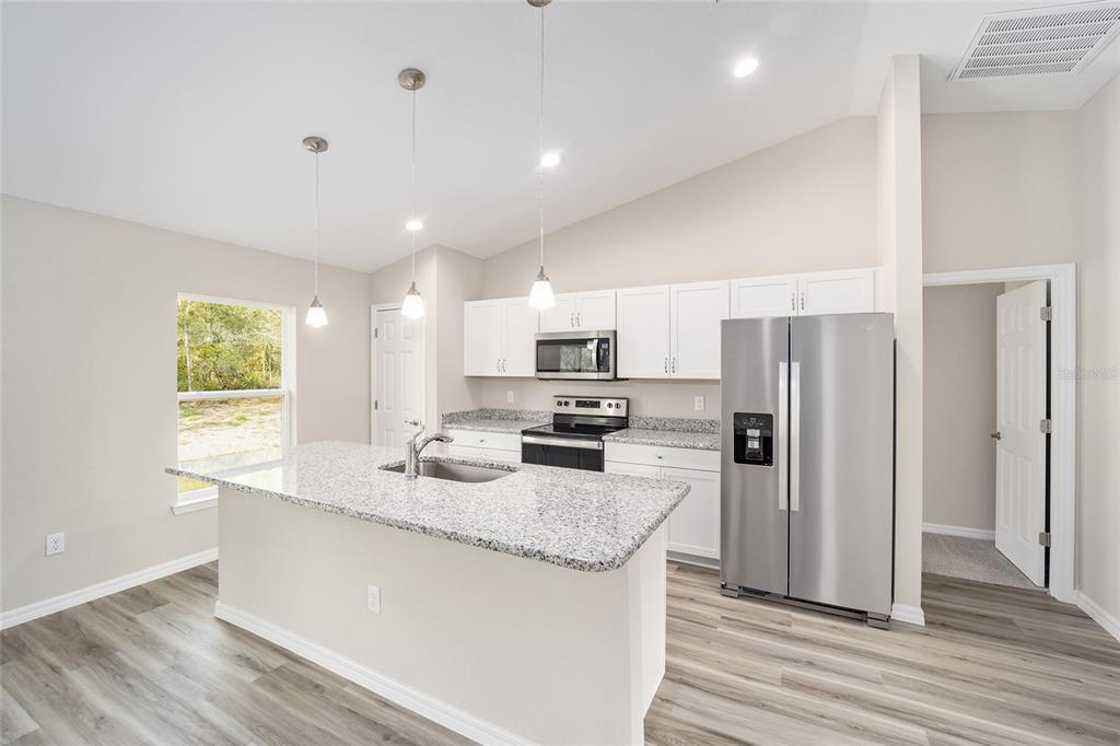A kitchen features a granite-topped island, stainless steel appliances, white cabinets, and light wood flooring — 12995 SW 89TH COURT, OCALA, FL