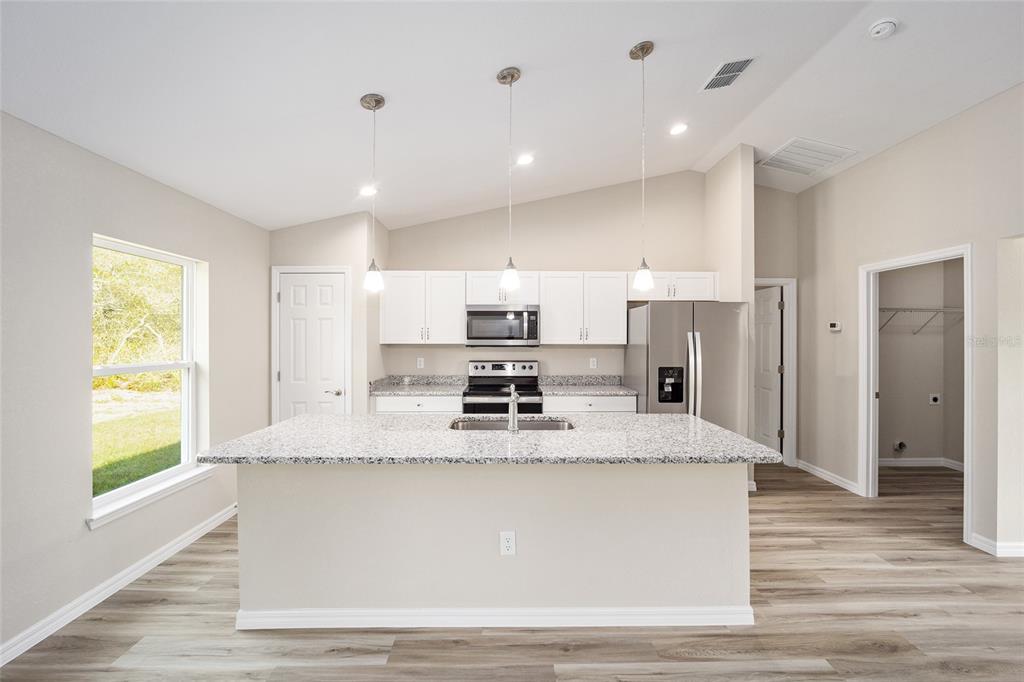 A kitchen features white cabinets, granite countertops, a center island, and stainless steel appliances — 12995 SW 89TH COURT, OCALA, FL