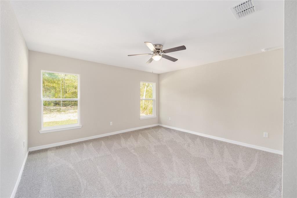 A bedroom with beige walls, gray carpet, two windows, and a ceiling fan — 12995 SW 89TH COURT, OCALA, FL